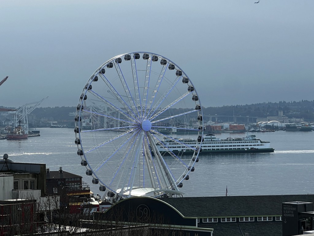 View of the Pier 57 Ferris wheel, a Bainbridge ferry coming to port, and the Seattle Aquarium from the Western Avenue Sky Bridge in Seattle. Image by JAG.