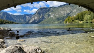 The Sava Bohinjka River rushes under a stone bridge with a beautiful view of Lake Bohinj from underneath.